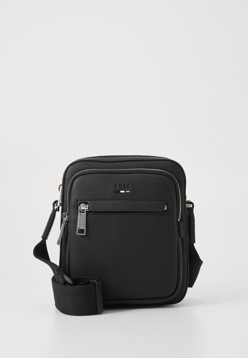 Bolso bandolera de cuero negro con una superficie texturizada, compartimento principal con cremallera, bolsillo frontal y correa ajustable. Acabados en hardware plateado.