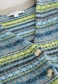 Strikket cardigan med blå, grønne og beige geometriske striber, beige knapper og et mærke med teksten "NEXT Made in China."