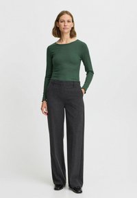 Langärmliges, geripptes grünes Shirt kombiniert mit dunkelgrauen, weit geschnittenen Hosen. Beide Teile weisen eine taillierte Silhouette und eine glatte Stofftextur auf.