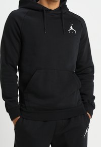Sudadera negra hecha de un tejido suave y texturizado. Cuenta con un bolsillo tipo canguro, capucha con cordón y un logo de Jordan en blanco en el pecho.