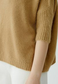 Brauner Strickpullover mit lockerer Passform, kurzen gerippten Ärmeln und einem strukturierten, weichen Stoff. Der Saum ist gerade und gerippt.