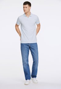 Polo de color azul claro con un cuello corto, combinado con unos vaqueros de mezclilla azules. El modelo lleva zapatillas blancas. Diseño simple y casual.