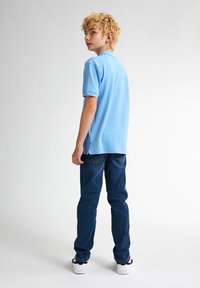 Světle modré polo tričko s límečkem, spárované s tmavě modrými džíny a bílými teniskami. Materiál vypadá měkký s hladkou texturou.