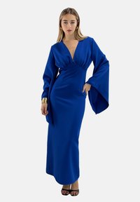 Lungo vestito blu con scollatura a V profonda, maniche larghe e vita aderente. Realizzato in tessuto morbido, presenta cuciture minime e drappeggiature intricate.
