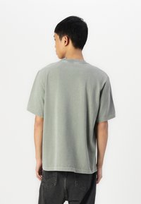 Camiseta de algodão cinza com um corte descontraído, mangas curtas e decote redondo. Textura suave com um leve efeito de lavagem vintage.