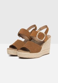 Brown suede wedge sandals with open toe, ankle strap, and a buckle closure. Jute-wrapped platform adds texture and height.