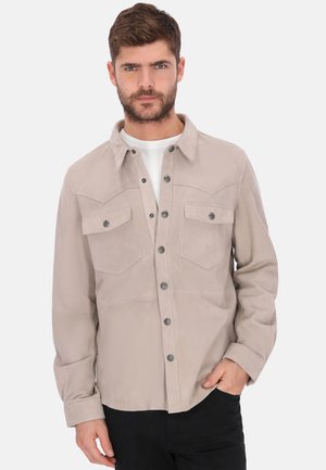 Beżowa zamszowa koszula-kurtka z zapięciem na guziki, dwie kieszenie na piersi, ozdobny karczek z ostrymi zakończeniami oraz długie rękawy. Srebrne guziki.