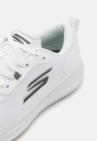 White athletic shoe with mesh upper, laces, and a padded collar. Features black logo accents and a textured rubber sole.