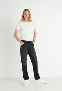 Camiseta blanca de cuello redondo combinada con unos vaqueros negros holgados y zapatillas blancas. Los vaqueros tienen una textura deslavada, con un diseño estándar de cinco bolsillos.