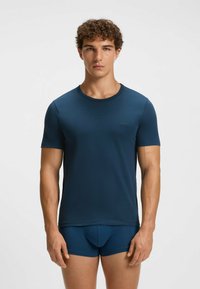 T-shirt in cotone blu navy con colletto a girocollo, maniche corte e un logo discreto sul petto, abbinato a slip coordinati.