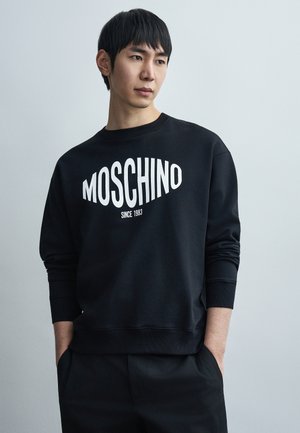 Hanorac negru cu logo "MOSCHINO" alb și textul "DIN 1983". Dispune de manșete canelate și design cu gât rotund. Textură moale, din țesătură solidă.