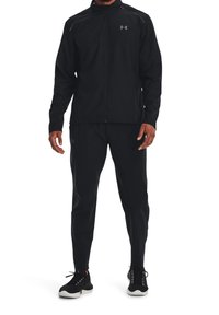 Completo da jogging maschile nero realizzato in tessuto leggero. La giacca presenta una chiusura con zip e dettagli riflettenti; i pantaloni hanno una vestibilità affusolata.