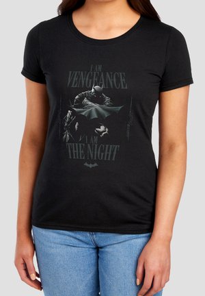 Frau trägt ein schwarzes T-Shirt mit Batman-Grafik und dem Text "I am vengeance, I am the night" in dunklen Tönen.