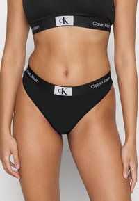 Bikini nero Calvin Klein, realizzato in un tessuto liscio, con taglio a vita media e una fascia con logo in bianco e grigio.