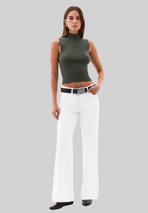 Strakke donker groene mouwloze top, witte wijde broek, zwarte riem met ronde zilveren gesp, gladde textuur, model staat op een grijze achtergrond.