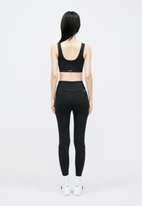 Fekete sportmelltartó és magasderekú leggings, mindkettő sima anyagból. Fehér tornacipő logóval. A modellt hátulról mutatják.