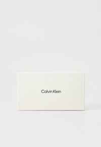 Bijela pravokutna kutija s matte finišem, sa nazivom branda "Calvin Klein" u modernom crnom fontu centriranom na prednjoj strani.
