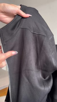 Pelēks jaku ar rāvējslēdzēju, veidotu no gludas, elastīgas auduma. Iespējas ietver augstu apkakli un vīļu detaļas. Rāvējslēdzējs stiepjas gar priekšpusi, nodrošinot vieglu uzvilkšanu.