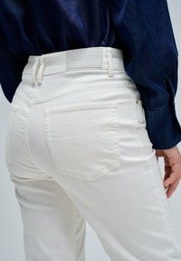 Gros plan sur une personne portant un jean blanc Salsa et une chemise en denim bleu marine, montrant la poche arrière et les passants de ceinture.