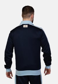 Marine trainingsjack met lichtblauwe accenten, voorzien van een kraag, ritsluiting en een textuurstof. Label zichtbaar op het nekgebied.