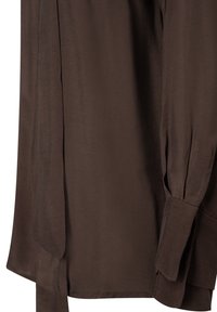 Bruine blouse met lange mouwen, voorzien van een gladde textuur, een ontspannen pasvorm en manchet mouwen. Inclusief een zijtouw voor een extra ontwerpelement.