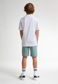 Chemise polo blanche et short vert clair. Chaussettes blanches à rayures noires et baskets noires et blanches. Design décontracté avec des manches courtes.