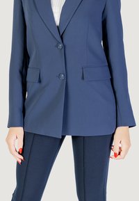 Blazer sartorial blu navy con due bottoni, colletto a rever e tasche frontali. Abbinato a leggings blu navy con cuciture laterali testurizzate.