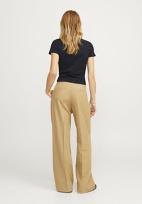 Zwarte, aansluitende top met korte mouwen, gecombineerd met hooggerokte, brede beige broek met achterzakken en een gladde textuur.