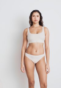 Beige intimatesett bestående av en bh med scoop-hals og lavt snitt bikiniundertøy. Mykt materiale med en glatt tekstur og minimalistisk design.