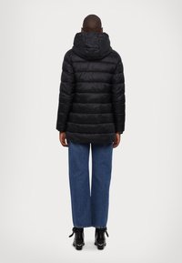 Chaqueta acolchada negra con capucha, con acolchado horizontal. Combinada con jeans de pierna ancha azules y botas negras de tacón.