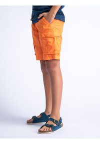 Felle oranje cargoshorts met meerdere zakken, met een comfortabele pasvorm en knielengte. Gecombineerd met donkerblauwe sandalen met banden en gespen.