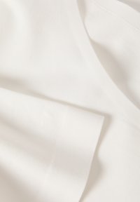 Tissu en coton blanc, texture lisse, présentant un design simple avec des plis et des drapés, affichant une apparence propre et neutre.