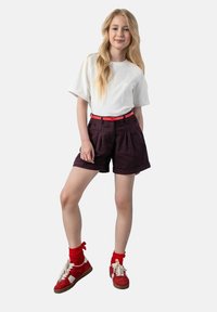 Biała koszulka z krótkim rękawem, spodenki w kratę w kolorze fioletowym z zakładkami, różowy pasek, czerwone trampki i pasujące czerwone skarpetki. Prosty, codzienny strój.