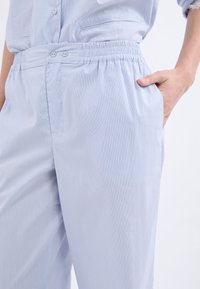 Pantalones a rayas azul claro con cinturilla elástica, bolsillos laterales y una textura suave. El patrón sutil añade interés visual.