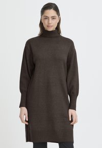 Barna kötött garbónyakú ruha hossz�ú ujjakkal, bordázott mandzsettákkal és laza szabással. A szövet puha és texturált hatású, a comb közepéig ér.