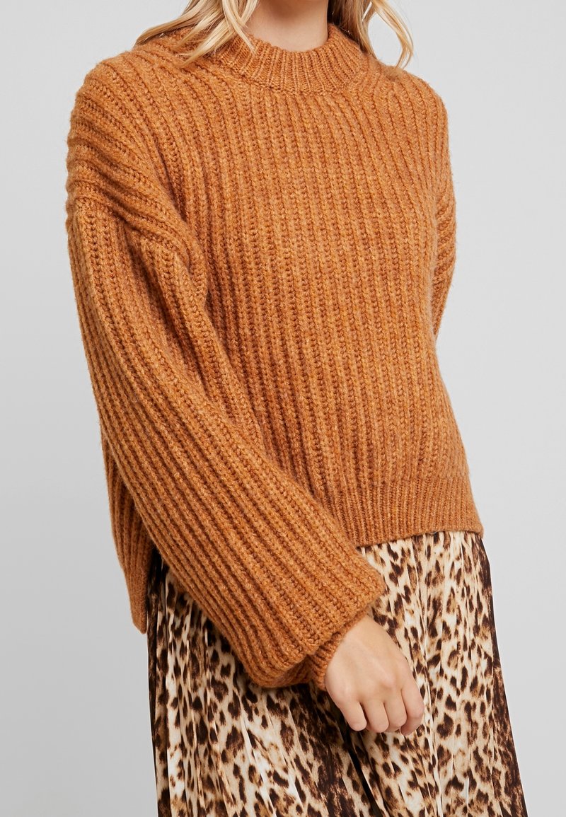 Sweter w kolorze rdzy z prążkowanego materiału, o wysokim dekolcie i szerokich, oversize'owych rękawach, w zestawie z spódnicą w deseń lamparta.
