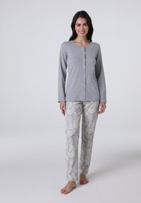 Maglietta grigia a maniche lunghe con chiusura a bottoni abbinata a pantaloni chiari a fantasia con design di foglie in tonalità di grigio e crema.