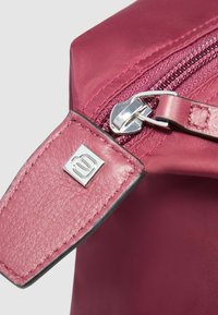 Donkerroze stoffen tas met een glanzende zilveren rits en een gestructureerd roze leren accent met een metalen logodetail.