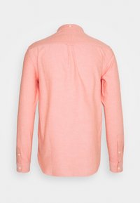 Lichtroze shirt met lange mouwen, gemaakt van een zachte, gestructureerde stof. Voorzien van een standaardkraag, knopen aan de voorkant en manchetten met één knoop.