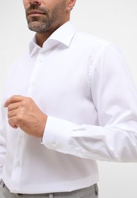 Witte dress shirt met een puntkraag, lange mouwen en knoopmanchetten. Gladde, lichte stof met een reguliere pasvorm. Geen patronen of versieringen.