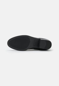 Semelle de chaussure noire en caoutchouc texturé pour une meilleure adhérence, forme arrondie et talon léger. Présente un branding minimaliste et une finition lisse.