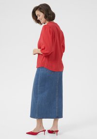 Röd texturerad blus med puffärmar, kombinerad med en lång denimkjol. Avslutad med röda högklackade mules och en böjd fåll på blusen.