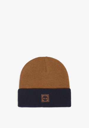 Bonnet en tricot bicolore marron et bleu foncé avec un revers plié comportant un patch en cuir carré cousu.