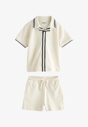 Chemise crème à manches courtes boutonnée avec des rayures bleu marine, associée à un short crème assorti à cordon de serrage.