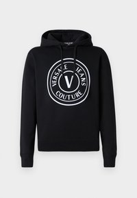 Must värvi kapuutsiga pluus pehmest kangast, millel on ümmargune valge logo, mis sisaldab "VERSACE JEANS COUTURE" ja silmapaistvat "V" keskel.