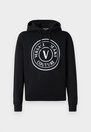 Black hoodie made of soft fabric, featuring a circular white logo that includes "VERSACE JEANS COUTURE" and a prominent "V" at the center.