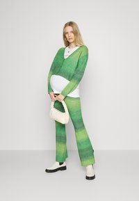 Cardigã verde em ombre e calças flare combinando em tecido de malha, usadas com uma blusa branca. Inclui uma carteira trançada branca e botas de tornozelo.