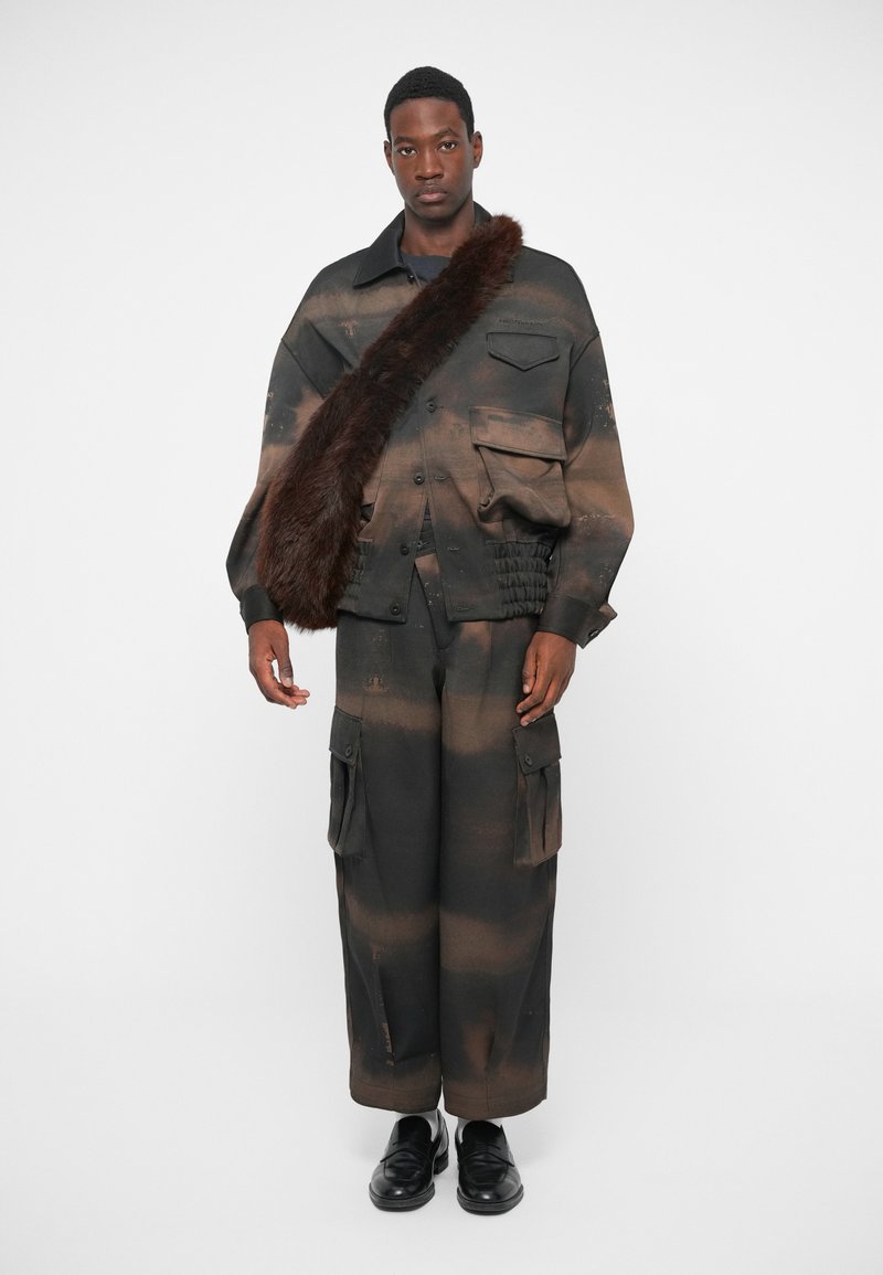 Insieme di moda composto da una giacca a motivi marroni e neri con tasche, abbinata a pantaloni cargo a gamba larga coordinati. Accentuato con pelliccia sintetica.