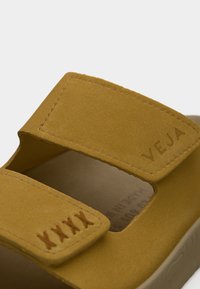 Κίτρινο δερμάτινο σανδάλι με λουράκια Velcro και ραμμένες λεπτομέρειες. Διαθέτει διαμορφωμένο πέλμα και ελαφριά σόλα. Εμφανές το λογότυπο της μάρκας.