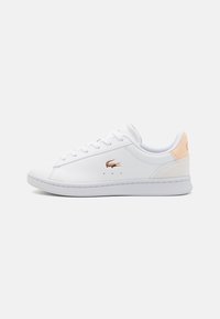 Fehér sneaker sima bőr felsőrésszel, kerek orral és fűzős rögzítéssel. Finom rózsaszín részlet található a saroknál és egy fényes logó.